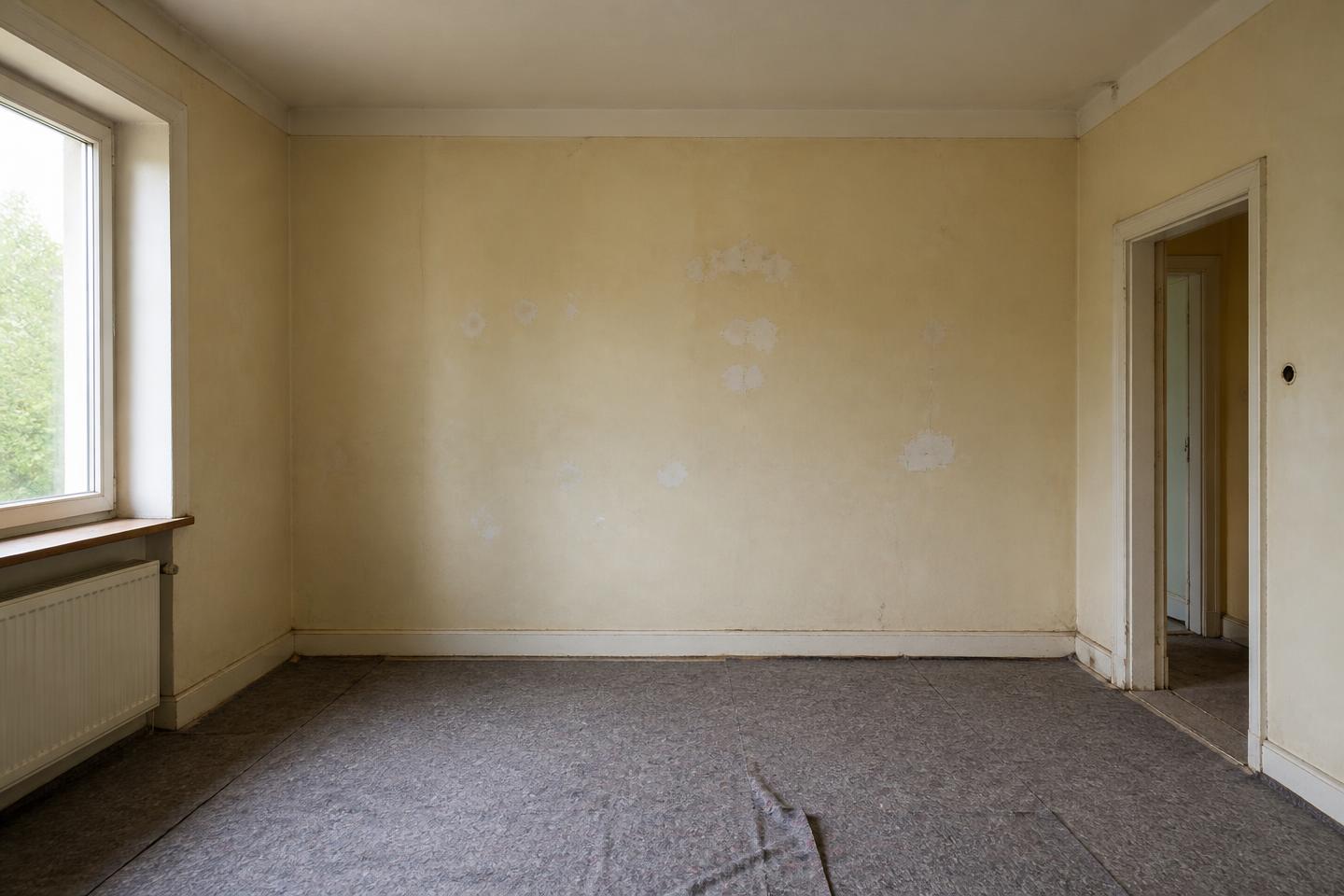 Wohnraum vor der Renovierung mit vergilbten Wänden, Rissen und Abdeckvlies